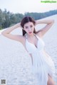 A woman in a white dress posing on a beach.