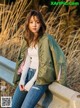 a woman sitting on a wall wearing a green jacket and jeans