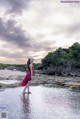 A woman in a red dress standing in the water.