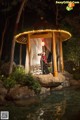 A woman standing in front of a gazebo in the middle of a pond.