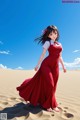 A woman in a red dress walking in the sand.