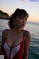 A woman in a red dress standing by the water.