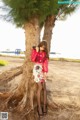 A woman leaning against a tree on the beach.