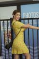 A woman in a yellow dress leaning against a fence.